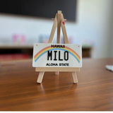 Personalized 4x2 inch mini Hawaii state license plate displayed on a wooden tripod stand for product presentation