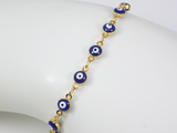 Blue evil eye bracelet worn on the wrist, showing the delicate gold‑plated chain and small enamel charm
